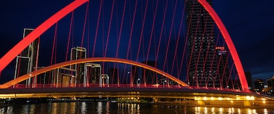 Imagen nocturna de un paisaje urbano con un puente rojo iluminado en primer plano